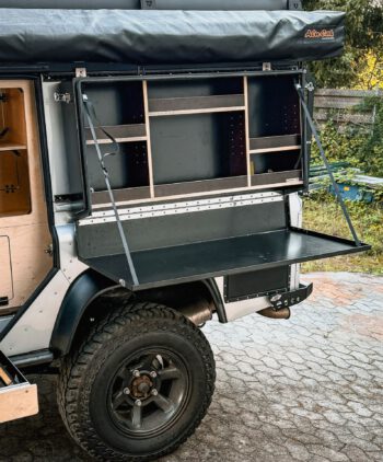Seitenbox für Defender, Defender Küchenbox, Defender Offroad-Kitchen, Defender Offroad-Küche, Defender Stauraumbox, Defender Werkzeugbox, Defender Klapptisch, aus Aluminium, schwarz matt pulverbeschichtet, am Fahrzeug befestigt, geöffnet, mit Regalböden